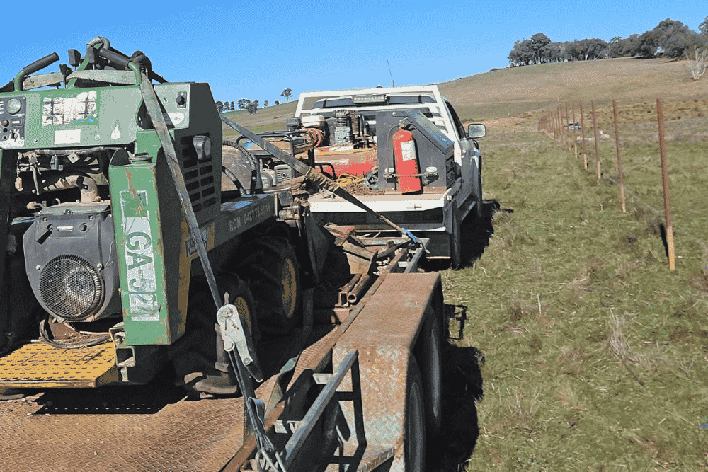 Work trailer loaded with professional fencing machinery parked next to a newly installed post line-